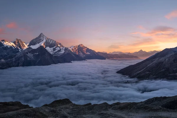 Schneebedeckte Berge erheben sich aus einem Meer aus Nebel unter einem farbenprächtigen Himmel bei Sonnenaufgang