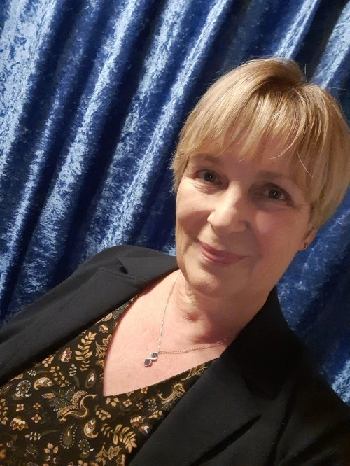 Porträt einer lächelnden blonden Frau in schwarzem Blazer vor blauem Hintergrund