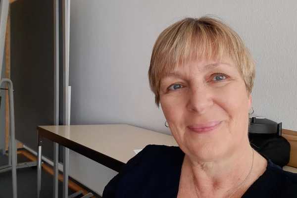 Blondhaarige Frau lächelt in einem Büro leicht unscharf im Hintergrund