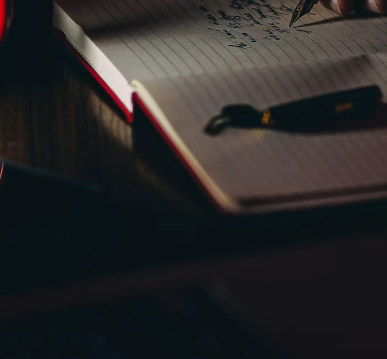 Notizbuch mit handschriftlichen Einträgen und dunklem Stift aufgenommen in gedämpftem melancholischem Licht