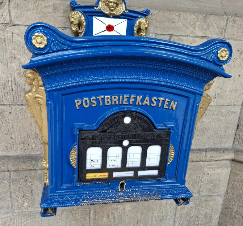 Königlichblauer historischer Postkasten mit goldenen Verzierungen an einer Steinwand