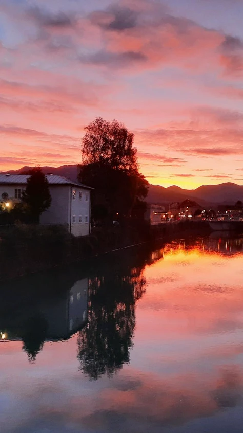 Spiegelung von Gebäuden und Bäumen bei einem farbenprächtigen Sonnenuntergang über dem Wasser
